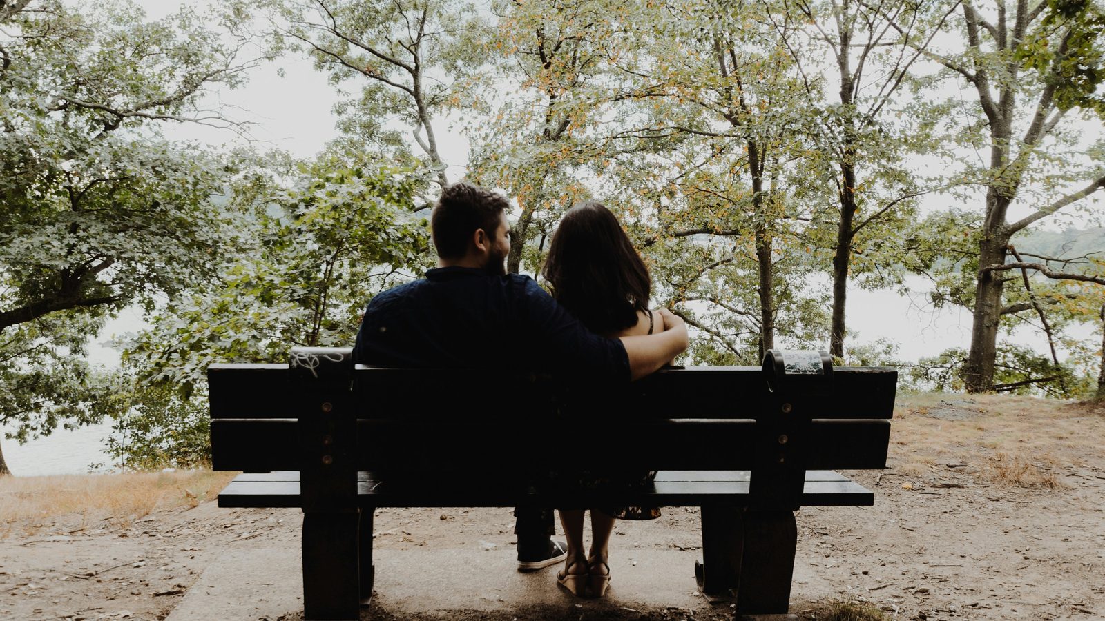 A husband and wife sitting together on a bench, looking out over the water.